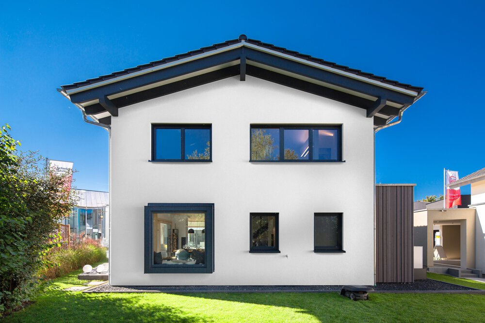 Ein modernes weißes Haus mit Satteldach, großen blauen Fenstern und einem kleinen Garten im Vordergrund.