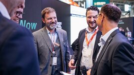 Mehrere Männer unterhalten sich an einem Messestand.
