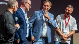 Four men on stage at EXPO REAL 2026, two holding microphones, engaged in lively discussion and smiling before a dark event backdrop.