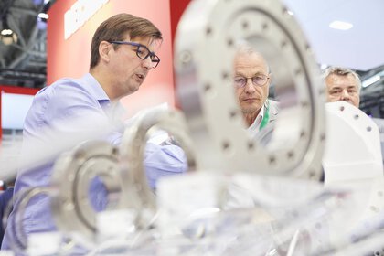 People inspecting ball bearings on display at a trade fair stand.