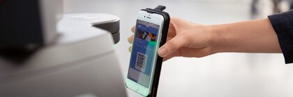 Eine Person hält ein Smartphone mit angezeigtem QR-Code an den Scanner einer Ticketschranke.