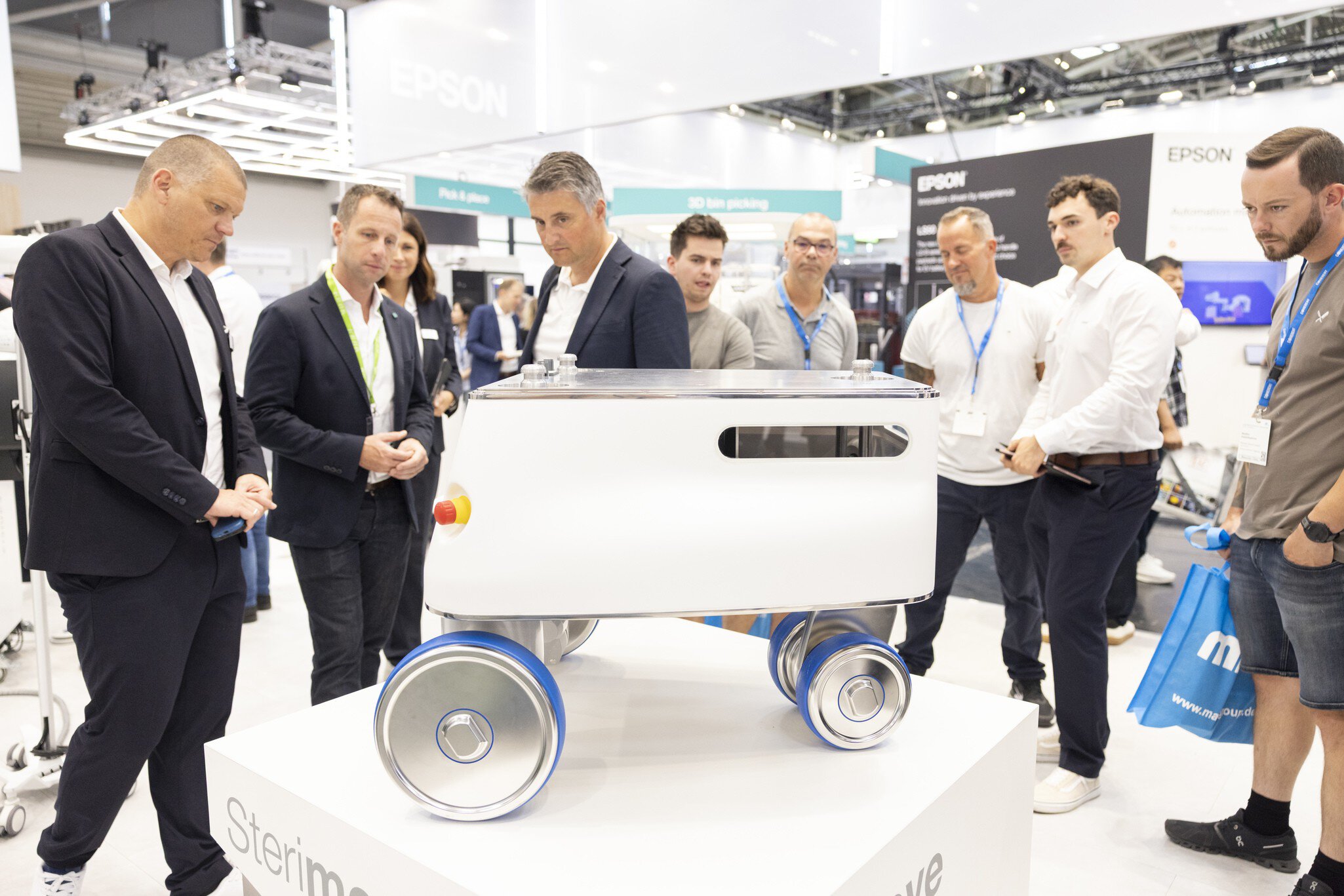 Gruppe von Männern betrachtet weißen Roboter auf Rädern bei Messepräsentation.