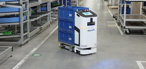 A white and black transport robot labelled ‘rexroth’ transports three blue crates in a warehouse with many full shelves.