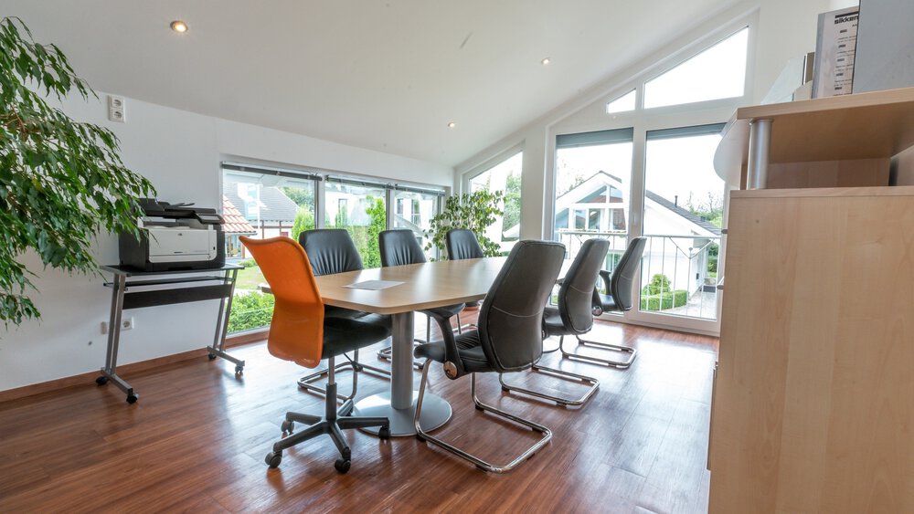 Ein moderner Konferenzraum mit einem langen Tisch, mehreren Stühlen, großen Fenstern und Pflanzen.