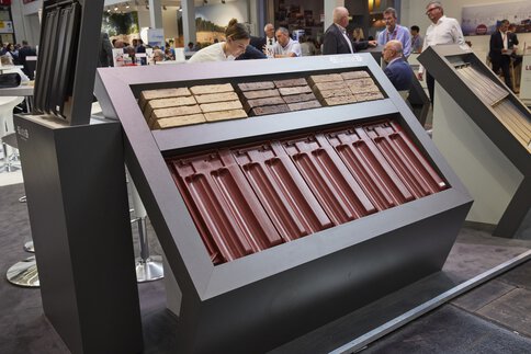 Exhibition of various building materials in front of a trade fair stand, people in the background.
