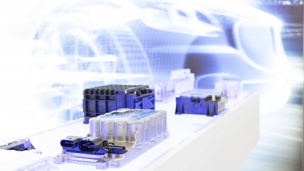 Energy cells displayed on a bright white pedestal, behind them is a wall graphic with a bright white grid of a car.