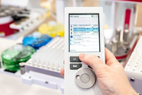 Handheld-Gerät mit Bildschirm, der eine Liste von Elementen anzeigt. Der Hintergrund ist unscharf und zeigt eine Laborumgebung.