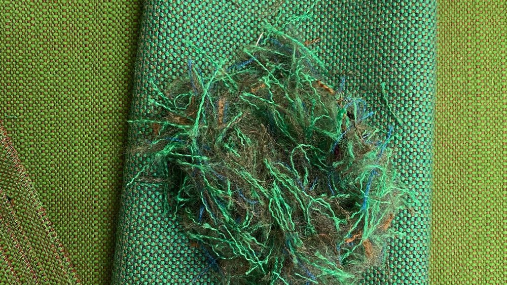 Grüne gewebte Stoffproben liegen übereinander, darauf ein Knäuel aus recycelten grünen und blauen Textilfasern