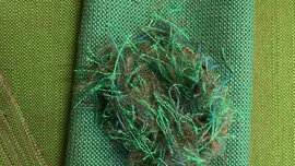 Grüne gewebte Stoffproben liegen übereinander, darauf ein Knäuel aus recycelten grünen und blauen Textilfasern