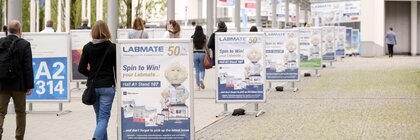 Überdachter Weg zur Messe München mit Aufstellern und Plakaten von Ausstellern auf der analytica 2024