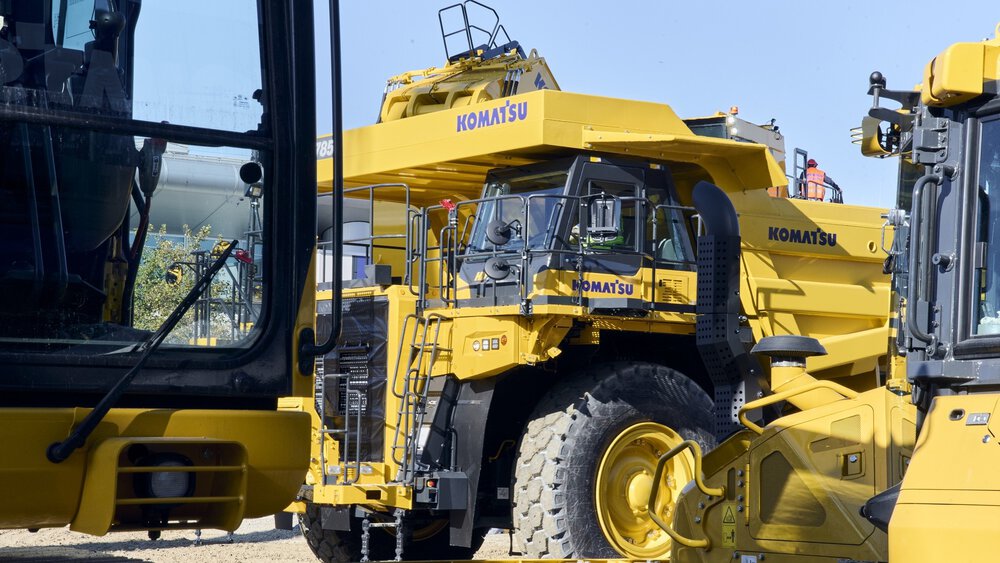 A yellow rigid frame dump truck from ‘Komatsu’ stands between other yellow vehicles on the open-air site of Messe München during bauma 2025.