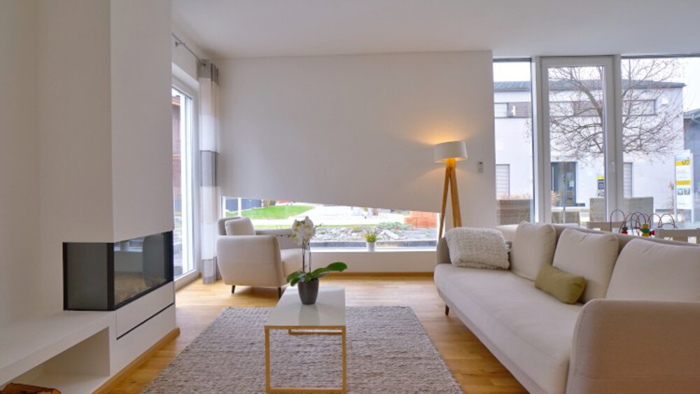 Modernes Wohnzimmer mit großen Fenstern, weißem Sofa, Stehlampe, kleinem Tisch und einem Teppich auf Holzboden.