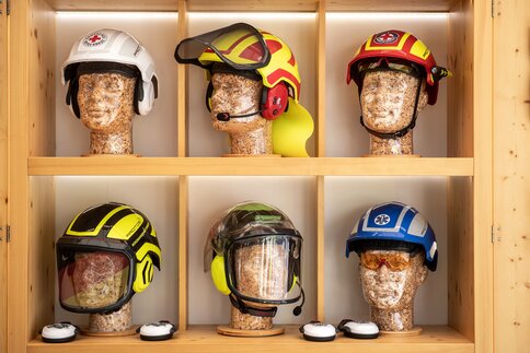 Various protective helmets for forestry and emergency use displayed on wooden shelves on mannequin heads.