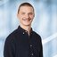 A man with short hair, a moustache and a dark corduroy shirt poses with a smile.