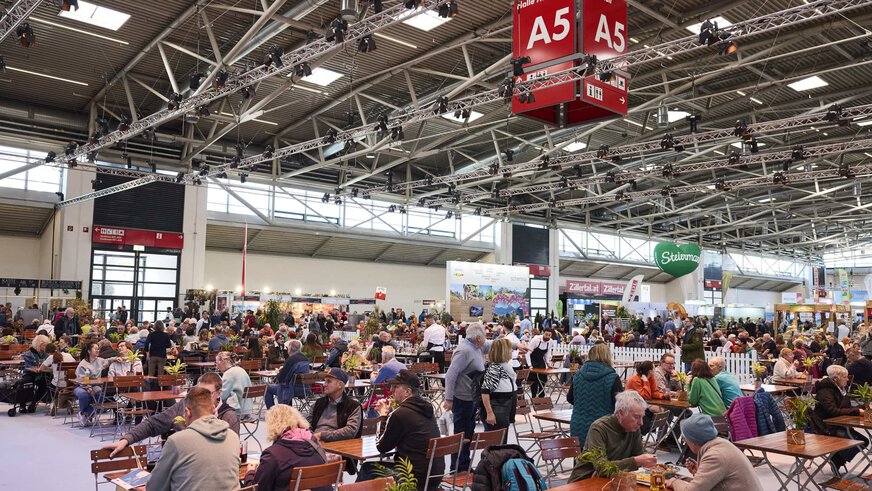 Large beer garden and catering area at the f.re.e trade fair in Hall A5 with numerous visitors at wooden tables, surrounded by stands and decorations.