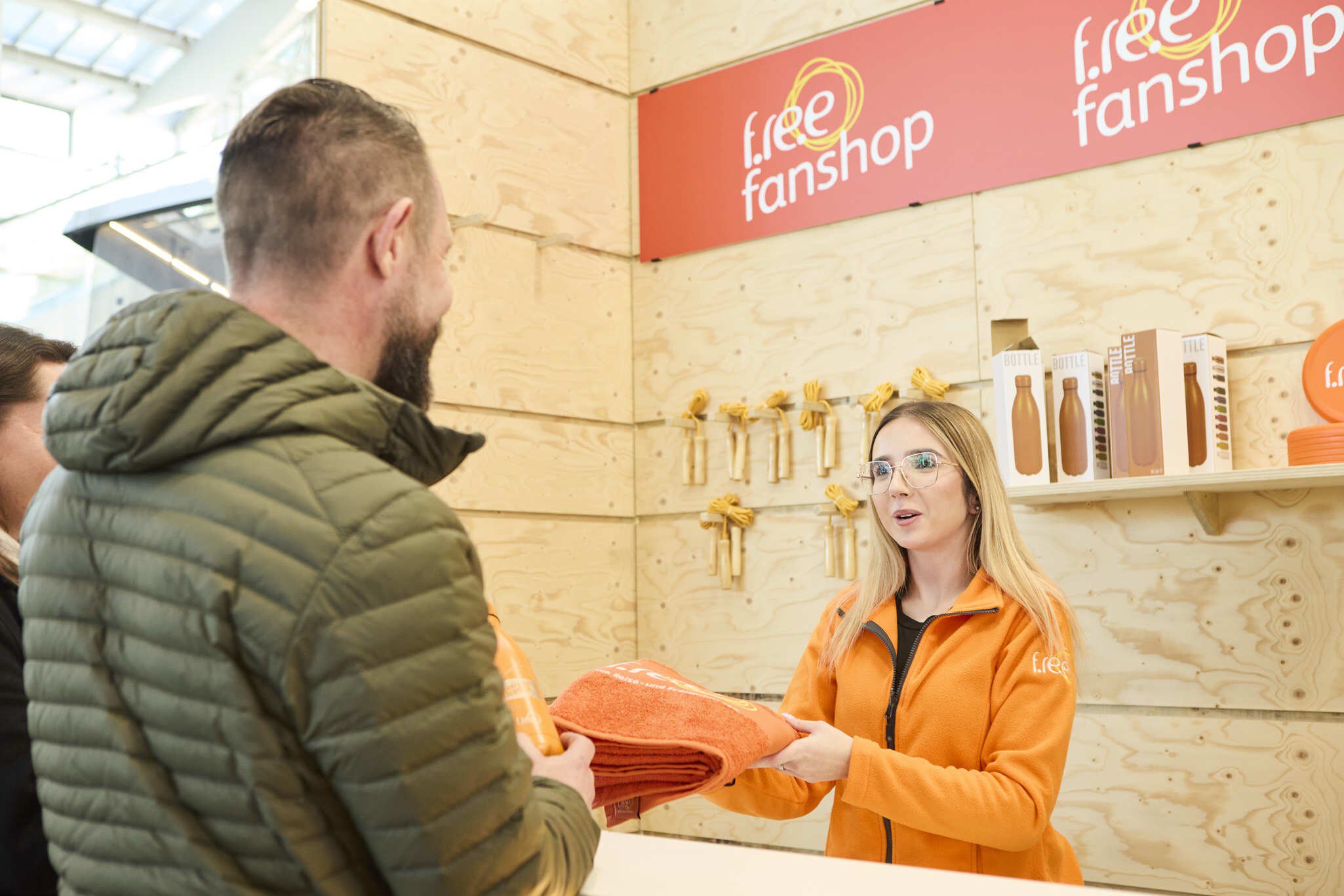 Verkauf von Merchandise-Artikeln am f.re.e-Shop in der Messehalle. Die Verkäuferin gibt im Verkaufsgespräch einem Käufer ein gebrandetes Handtuch.