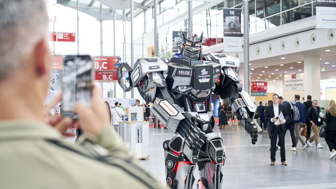 Shiny robot figure stands at the trade fair entrance, welcoming attendees.