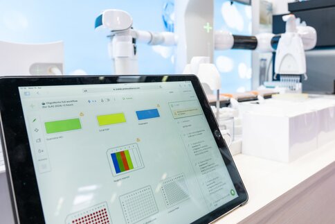 Tablet with laboratory software in front of a robotic system for automated laboratory diagnostics.