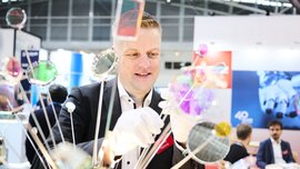Ein Aussteller präsentiert präzise optische Komponenten an einem Messestand auf der Laser World of Photonics 2025.