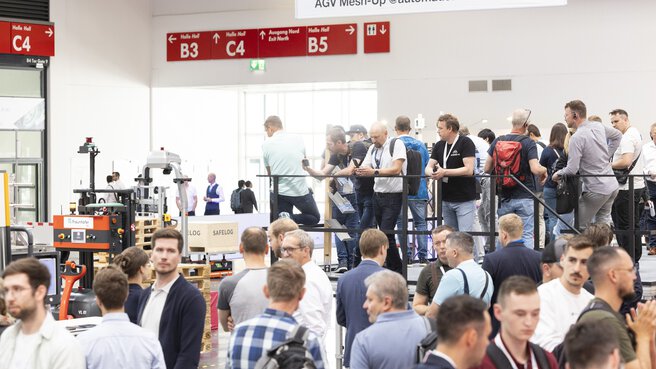 Crowd of people during automatica in Hall B4. Some of the people are standing on a platform to watch a demonstration of robots.
