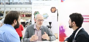 Three people talking at a stand for photonics and EU technology initiatives at a trade show.