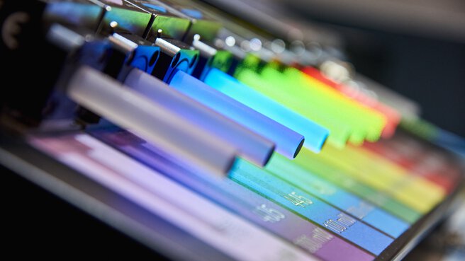 Close-up of several lasers with different wavelengths lined up, their attached diffusers glowing colorfully.