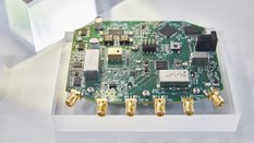 A circuit board with electronic components and several analog connections, presented on a Plexiglas cube at an exhibition stand.