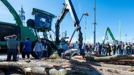 Ein grüner Forstharvester mit einem langen mechanischen Greifarm, der auf einer Fachmesse für Outdoor-Ausrüstung gefällte Baumstämme bearbeitet.