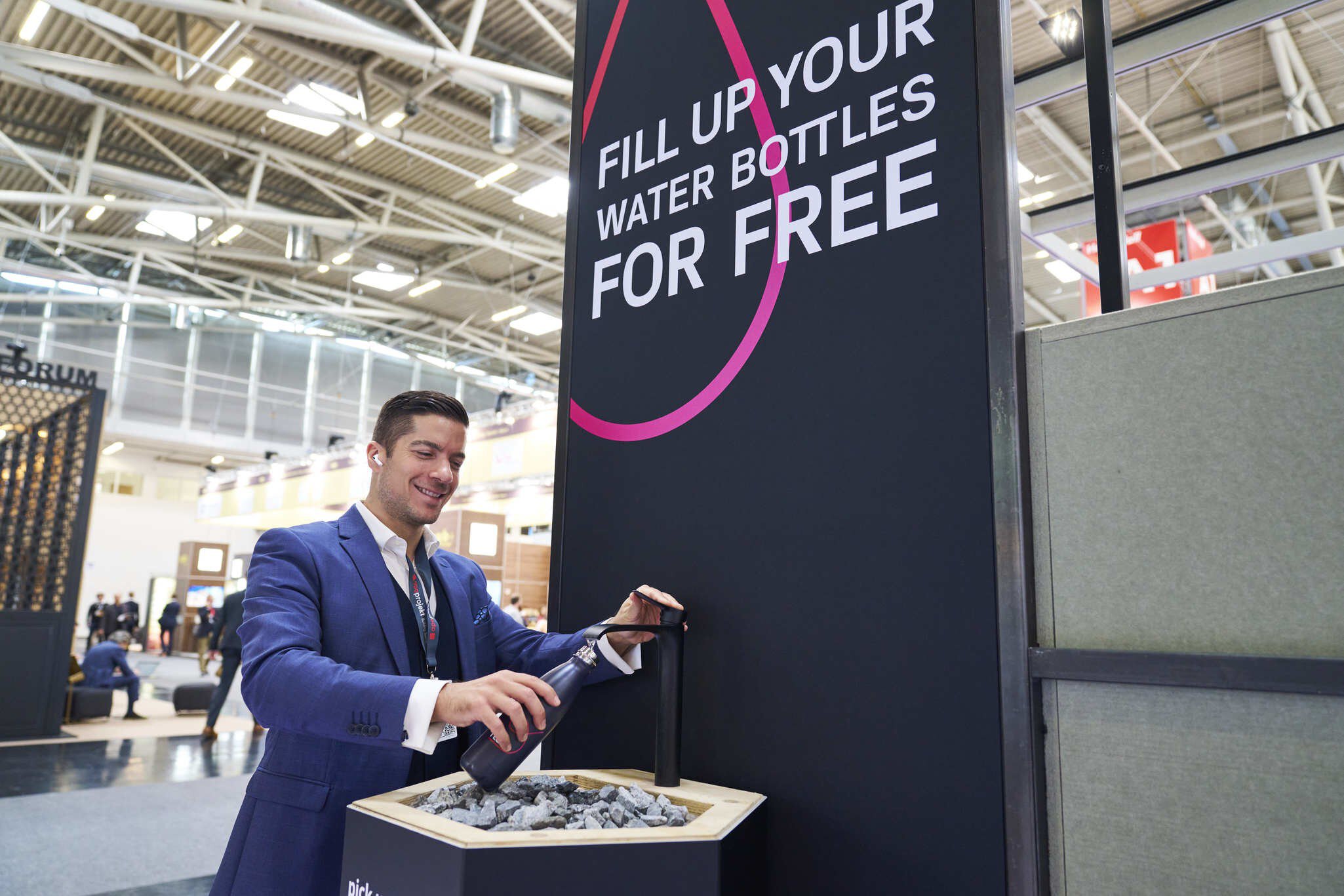 Man in suit fills water bottle at a free refill station with a large sign above him.