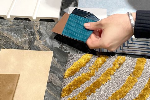 Eine Hand hält mehrere Stoffmuster über einen Tisch mit Marmor- und Textilmustern.
