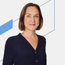 Frau mit kurzen braunen Haaren in einer dunklen Bluse, stehend vor einem weißen Hintergrund mit blauen geometrischen Linien.
