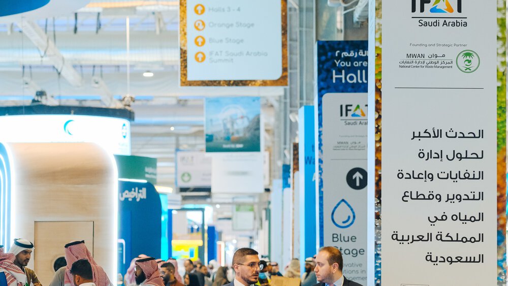  View of numerous advertising banners for various providers in a well-attended exhibition hall at IFAT Saudi Arabia.