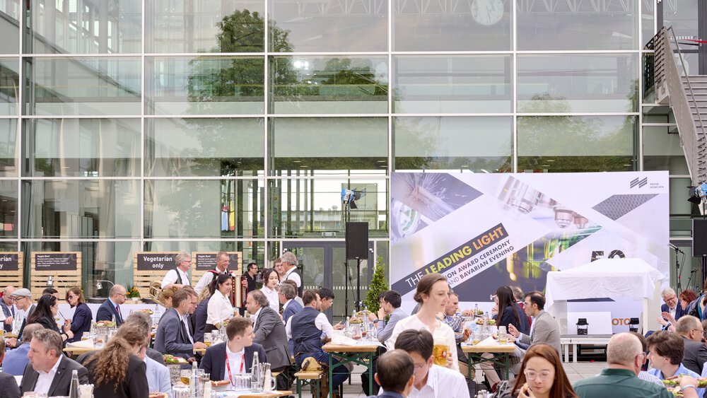 Eine Menschenmenge versammelt sich zum Essen an Tischen vor einer Messehalle. Im Hintergrund ist ein großes Schild der 