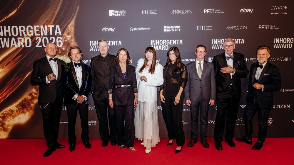 Nine people in festive attire stand together in front of a photo wall of the INHORGENTA AWARD 2026 and pose for a photo.
