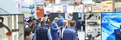 Zahlreiche Besucher, Messestände und Werbeschilder in der hell beleuchteten Messehalle A2.