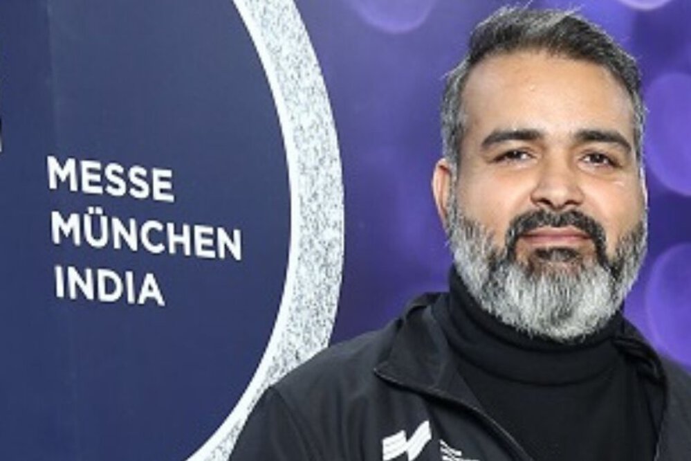 Bhupinder Singh vor dem Logo der Messe München India.