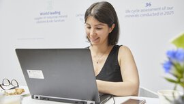 A woman in a black top is working on a laptop at a table with flowers.