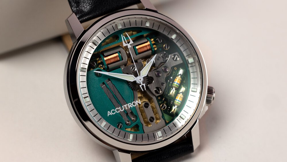 The close-up view of a small wristwatch with a glass face, a gray bezel, and black straps on display.