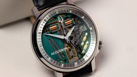 The close-up view of a small wristwatch with a glass face, a gray bezel, and black straps on display.