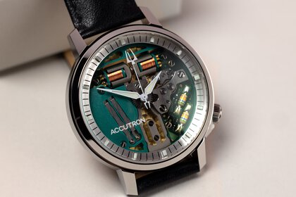 The close-up view of a small wristwatch with a glass face, a gray bezel, and black straps on display.