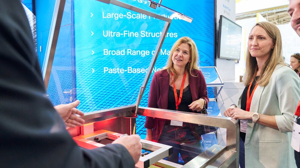 Two trade fair visitors watch a live demonstration on a machine with interest.