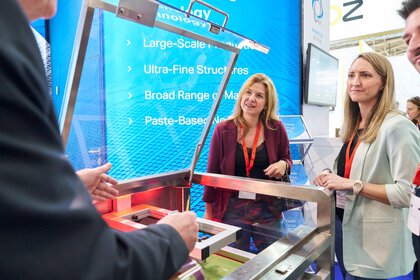 Two trade fair visitors watch a live demonstration on a machine with interest.