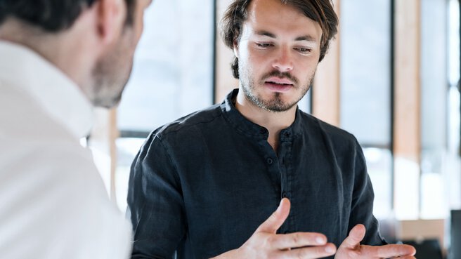 Two men are having a serious conversation in a building, one of them gesticulating with his hands.