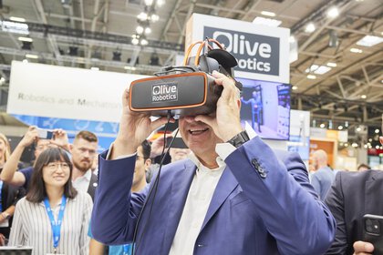 Mann, der bei einer Demonstration an einem Messestand durch ein Virtual-Reality-Headset schaut. Im Hintergrund sind Zuschauer.