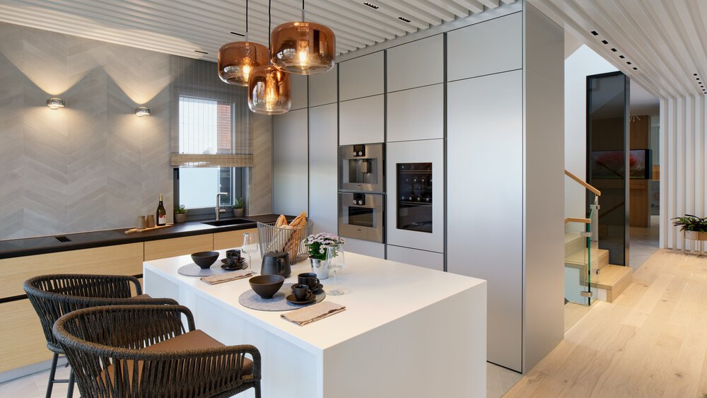 Moderne Küche mit Kochinsel, zwei Barhockern, hängenden Glaslampen und Einbaugeräten; Treppe im Hintergrund.