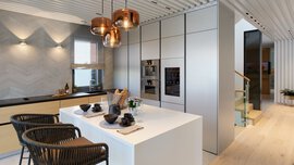 Moderne Küche mit Kochinsel, zwei Barhockern, hängenden Glaslampen und Einbaugeräten; Treppe im Hintergrund.