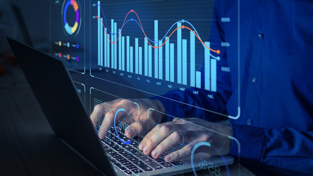 Person tippt auf einem Laptop, überlagert mit digitalen Diagrammen und Grafiken, die Datenanalysen und Statistiken zeigen.