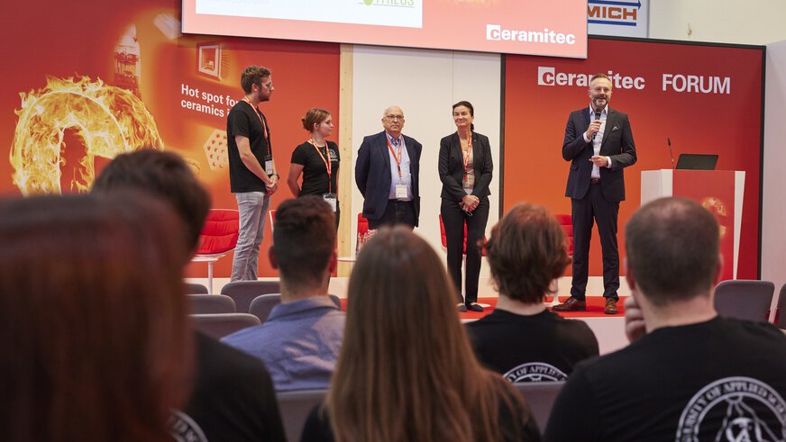 A panel of five people speaks on stage at a conference and is observed by the audience.