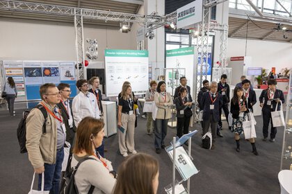 Eine Gruppe Menschen nimmt an einer Messeführung teil und verweilt vor einem Messestand.