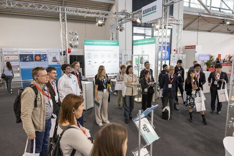 People attending the trade fair stand and look at a presentation area.